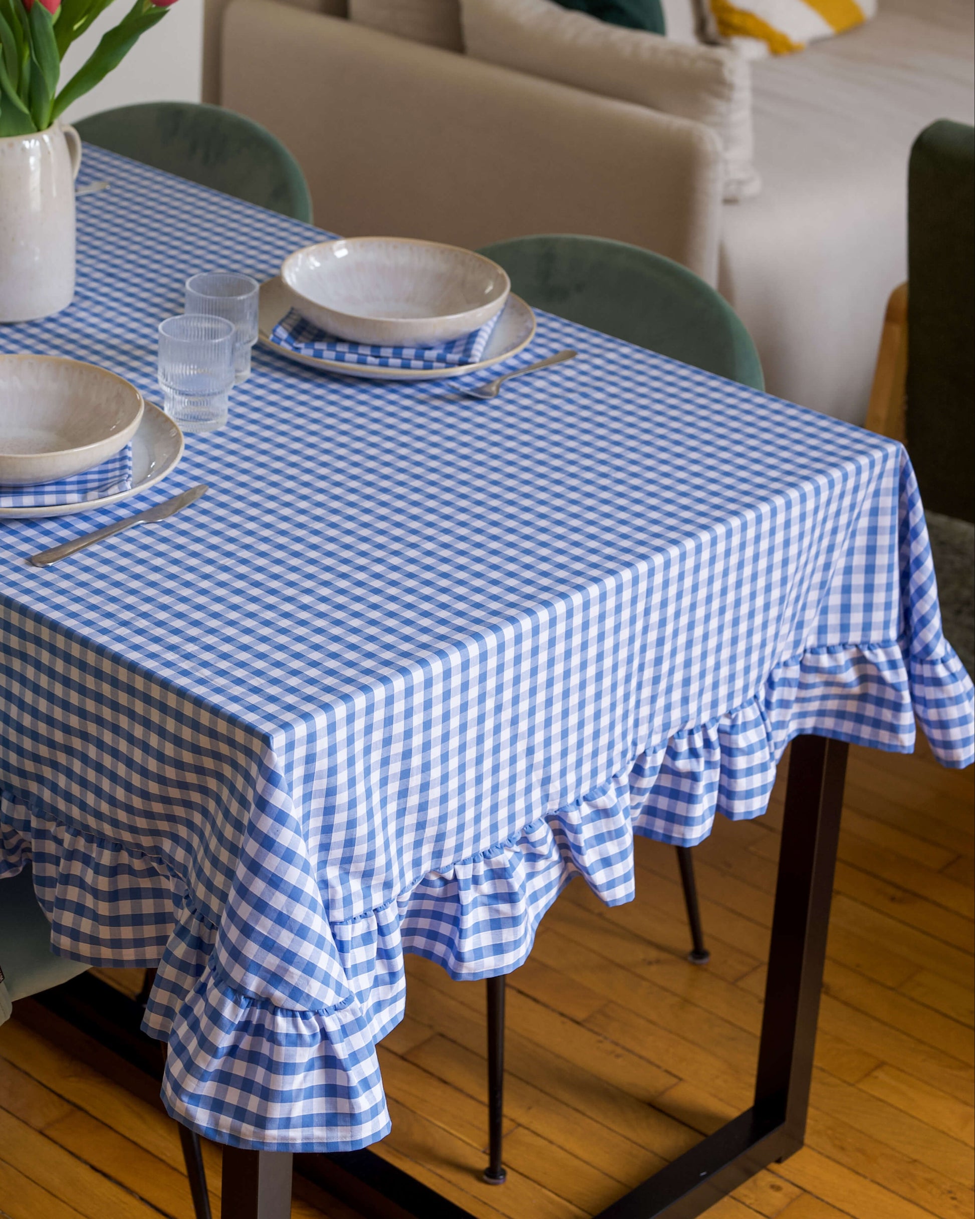 Gros plan sur le volant froncé de la nappe à carreaux bleu et blanc, en coton 100 % fabriquée à la main à Biarritz. Le tissu souple et le fini soigné soulignent le savoir-faire artisanal et le charme champêtre du modèle.