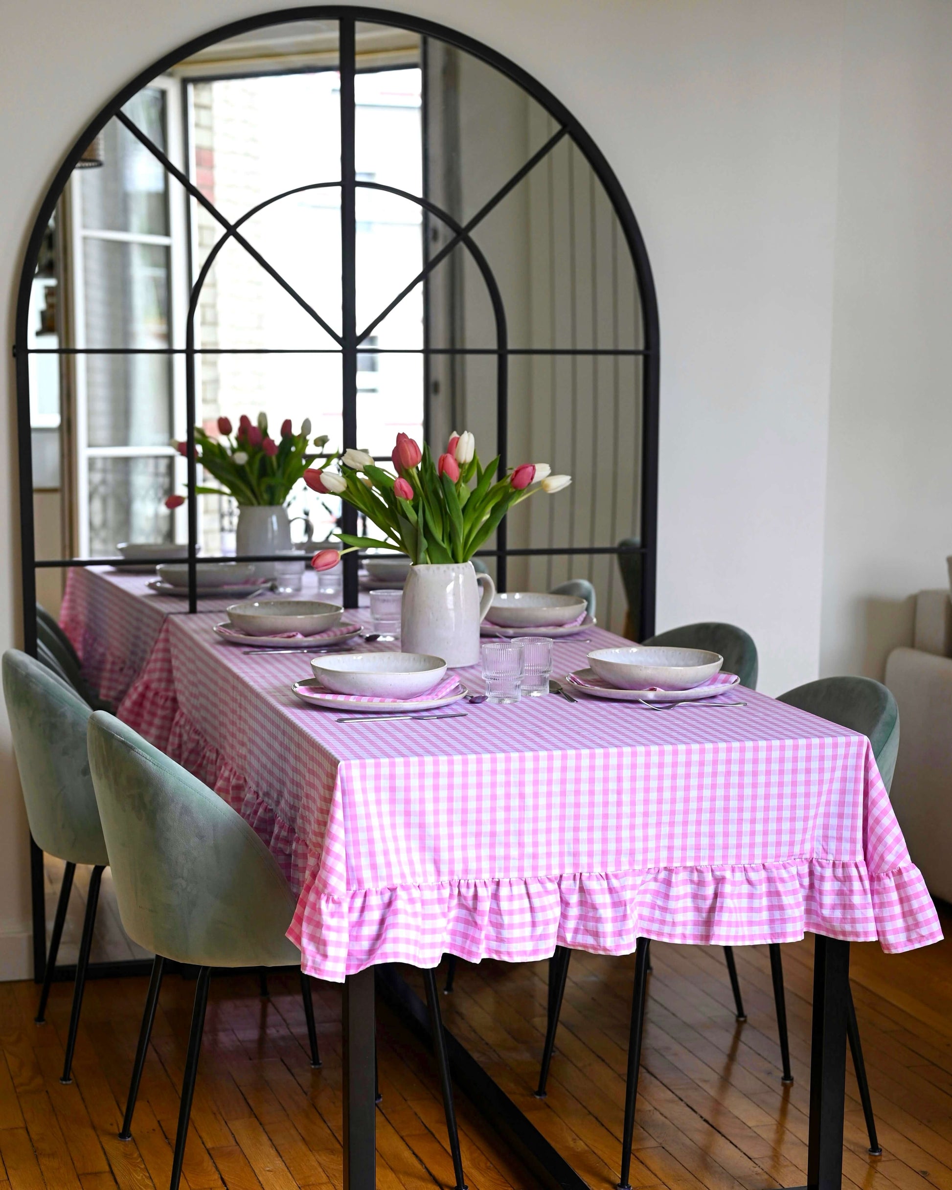 Nappe à carreaux rose et blanc avec volants, en coton 100 % fabriquée à la main à Biarritz, dressée sur une grande table de salle à manger avec vaisselle en grès et bouquet de tulipes, dans un intérieur lumineux et élégant.