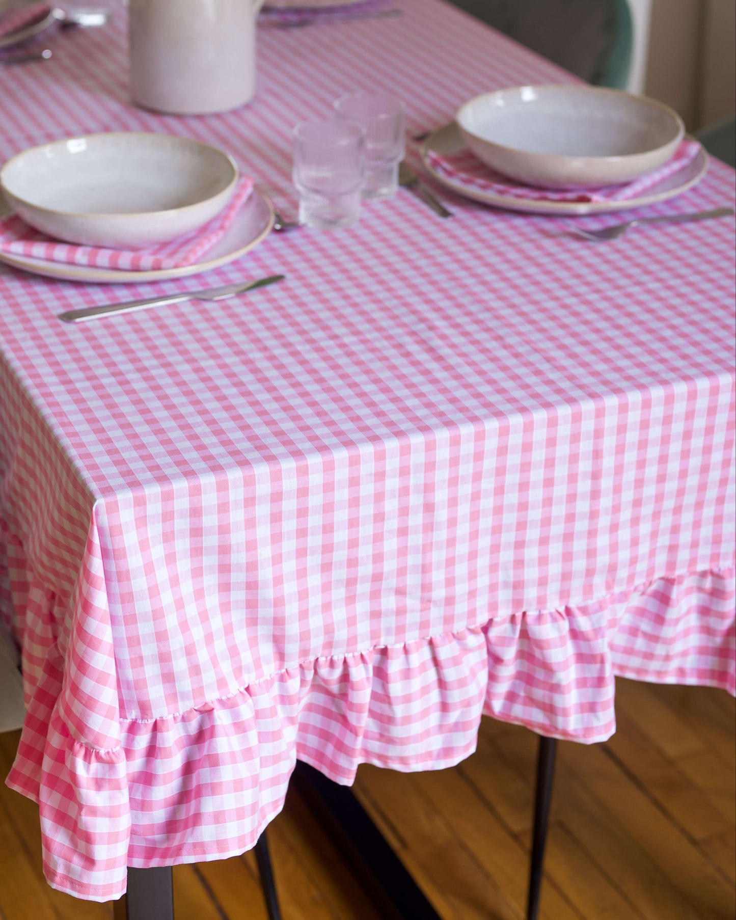 Gros plan sur le volant froncé de la nappe à carreaux rose et blanc, en coton 100 % fabriquée à la main à Biarritz. Le tissu souple et le fini soigné soulignent le savoir-faire artisanal et le charme champêtre du modèle.