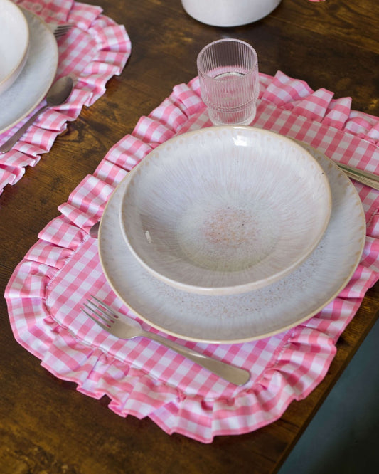 Set de table à carreaux vichy rose et blanc, en coton 100 %, avec finition matelassée et volant tout autour. Confectionné à la main à Biarritz, il ajoute une note élégante et accueillante à une table soigneusement dressée.