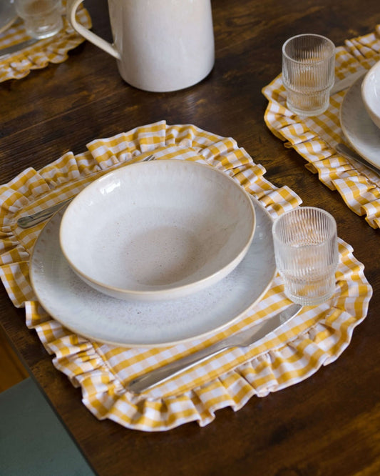 Set de table à carreaux vichy jaune et blanc, en coton 100 % avec finition matelassée et volant sur tout le contour. Fabriqué à la main à Biarritz, il apporte une touche raffinée et chaleureuse à une table joliment dressée.